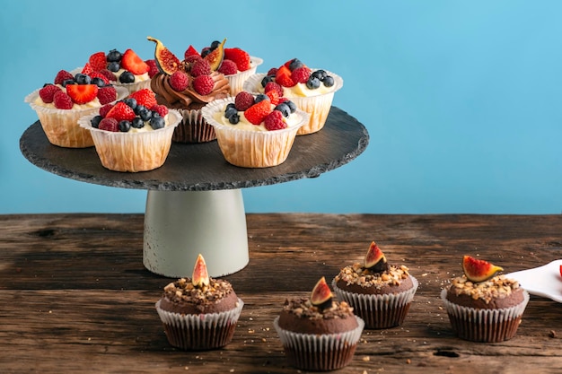 Muffin alla vaniglia e cioccolato con frutti di bosco freschi su sfondo blu Pasticceria in stand