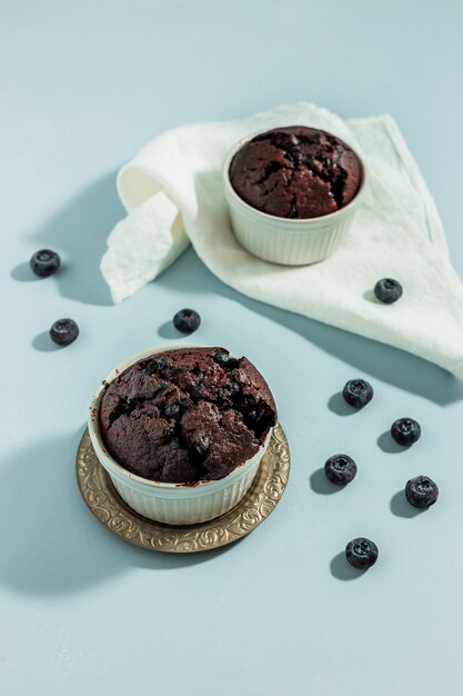 Muffin casalinghi della barbabietola al cioccolato con i mirtilli in tortiera bianca sulla superficie blu, tovagliolo bianco, colpo leggero duro