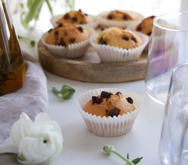 Muffin con crema e granelli di cioccolato su un supporto di legno vicino al ranuncolo bianco e una tazza di tè