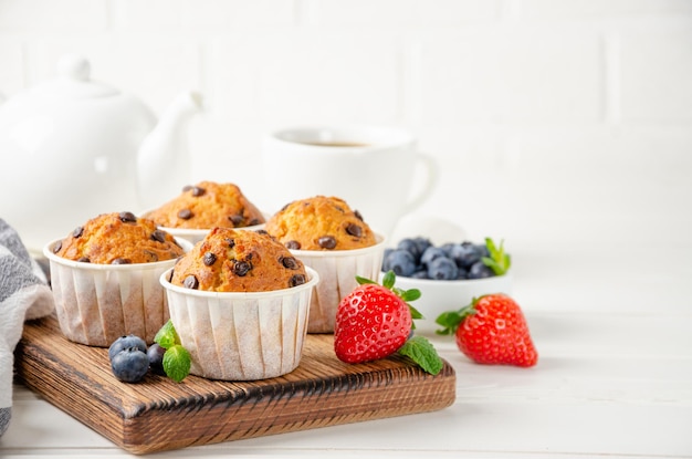 Muffin con gocce di cioccolato su un bordo di legno su uno sfondo bianco con frutti di bosco freschi. Copia spazio.