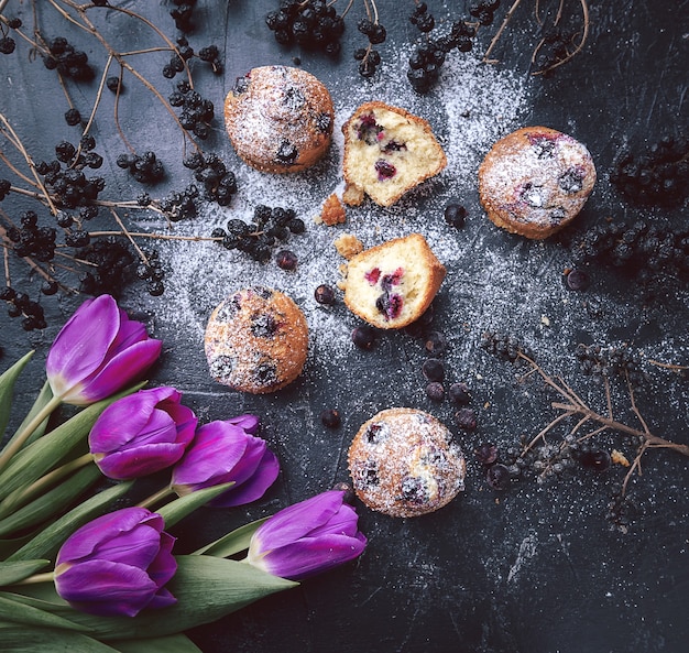 Muffin con ribes su uno sfondo scuro accanto alle bacche sui rami. e un mazzo di fiori. in stile rustico. stile scuro