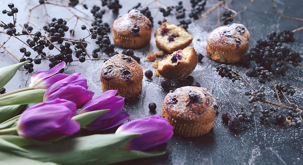 Muffin con ribes su uno sfondo scuro accanto alle bacche sui rami. e un mazzo di fiori. in stile rustico. stile scuro