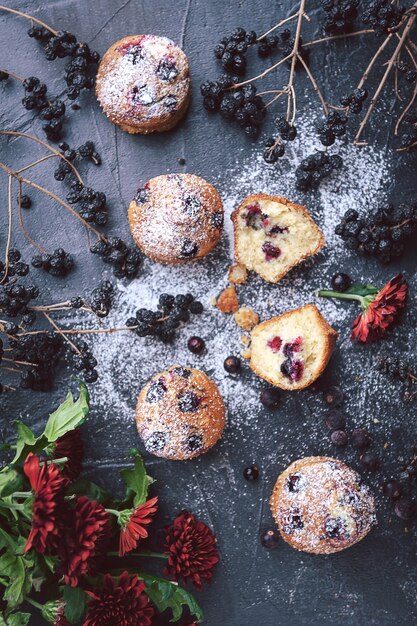 Muffin con ribes su uno sfondo scuro accanto alle bacche sui rami. e un mazzo di fiori. in stile rustico. stile scuro