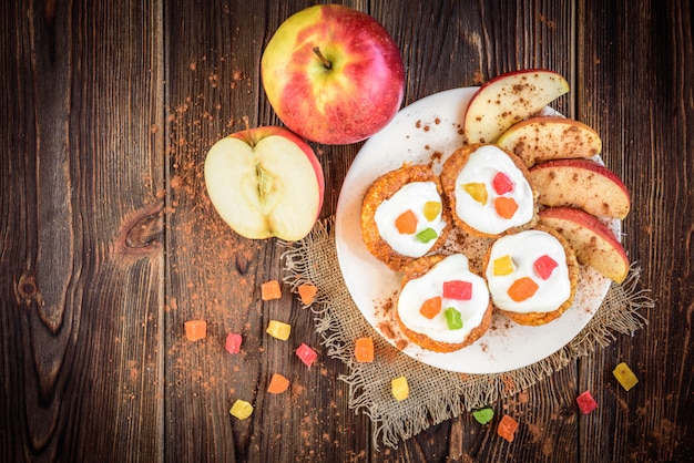 Muffin d'avena con yogurt, frutta candita, mela rossa e cannella su uno spazio di legno scuro.