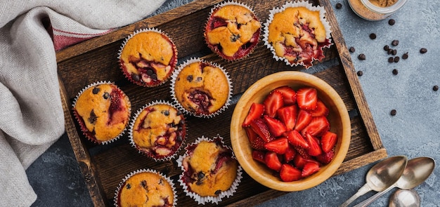 Muffin dei bigné del cioccolato della fragola sul vecchio supporto di legno su fondo grigio concreto. Vista dall'alto