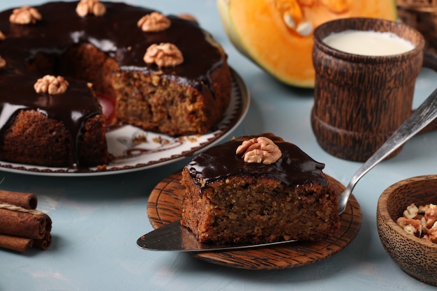 Muffin di zucca fatto in casa, con una fetta ritagliata, decorato con glassa al cioccolato e noci su una superficie blu chiaro, orientamento orizzontale