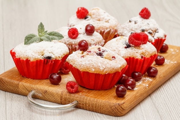 Muffin fatti in casa cosparsi di zucchero a velo e lamponi freschi su tagliere di legno