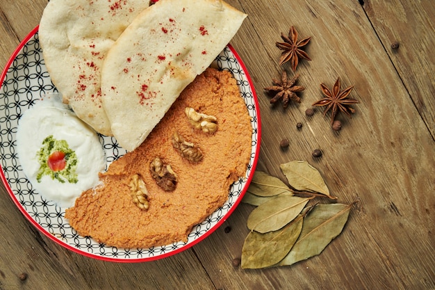 Muhammara è un classico piatto eastren. purea di pepe e noci al forno con bazlama e yogurt in un piatto di ceramica su una superficie di legno.