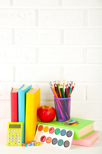 Multi libri di scuola e cancelleria colorati sul fondo bianco del muro di mattoni