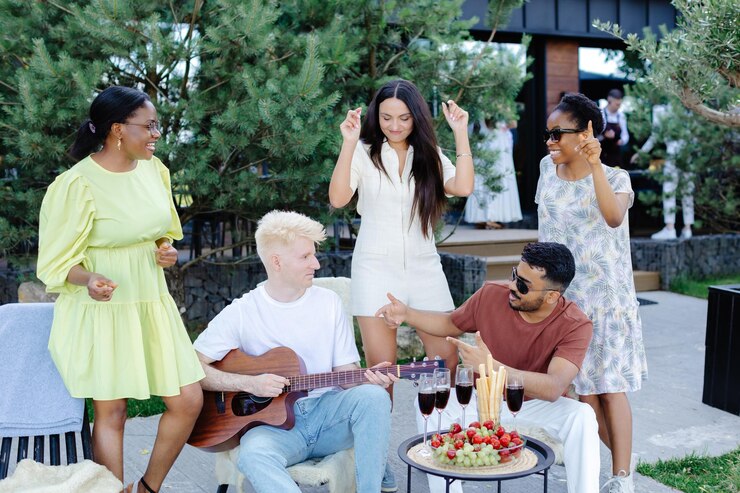 Multiracial group of friends is playing guitar singing songs at dinner party in summer picnic