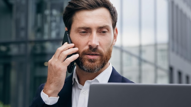 Multitasking uomo manager consulente parla al telefono consulenza cliente controlla le informazioni sul portatile