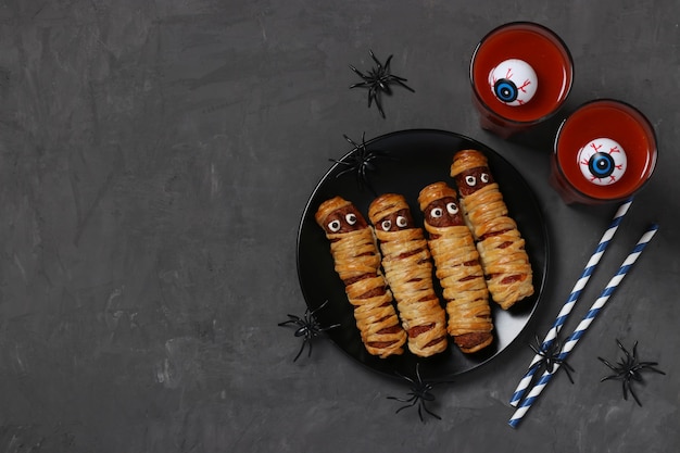 Mummie spettrali di salsiccia e succo di pomodoro per la festa di Halloween su piatto scuro, vista dall'alto. Disposizione piatta. Spazio per il testo.