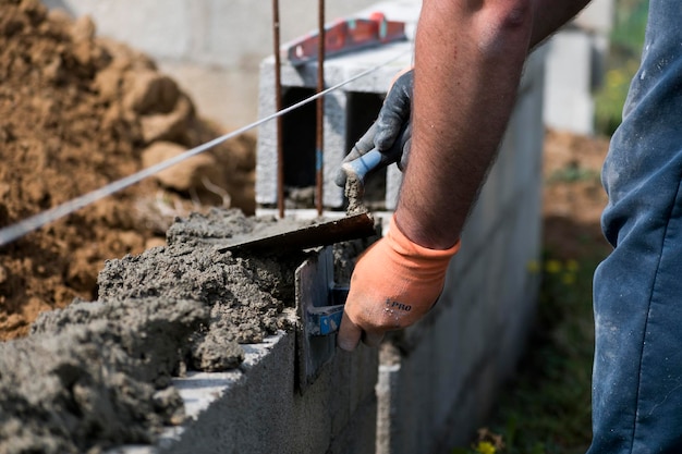 Muratore in guanto spargendo calcestruzzo per costruire un muro in cantiere