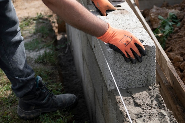 Muratore in guanto spargendo calcestruzzo per costruire un muro in cantiere