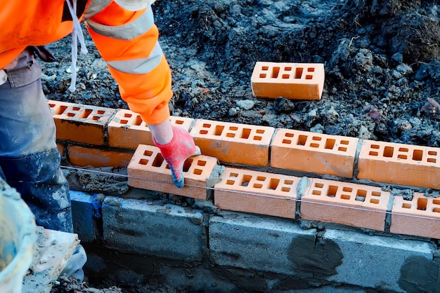 Muratore industriale che posa mattoni sulla miscela di cemento in cantiere Combattere la crisi abitativa