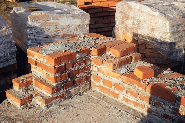 Muratura in mattoni con cemento su fondazione in calcestruzzo processo di costruzione di case Mattoni rossi per la posa su fondamenta in calcestruzzo Materiali da costruzione in cantiere
