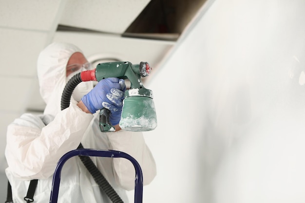 Muro di pittura lavoratore maschio con pistola a spruzzo in colore bianco tuttofare impegnato al lavoro