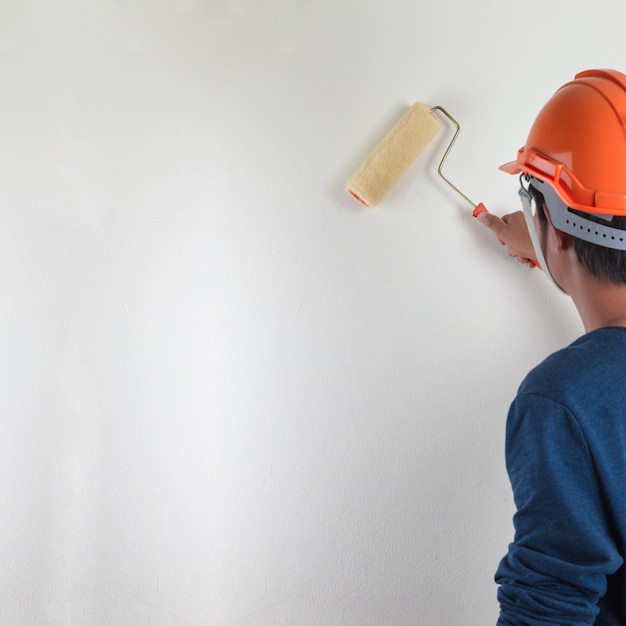 Muro dipinto a mano maschio con rullo di vernice, rinnovando con vernice di colore bianco.