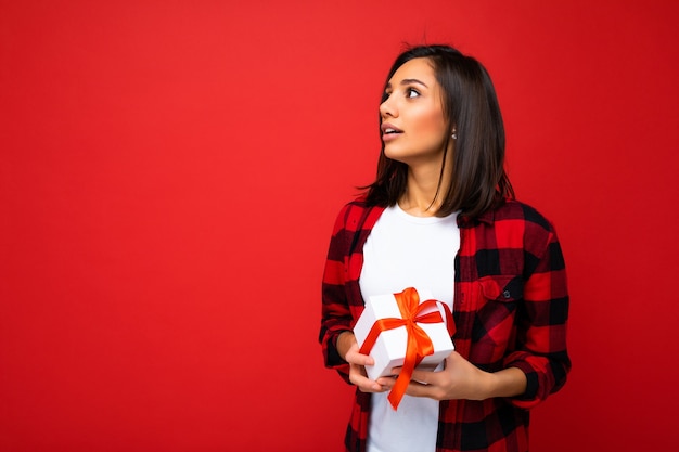 Muro isolato di una giovane donna bruna abbastanza positiva che indossa una maglietta casual bianca