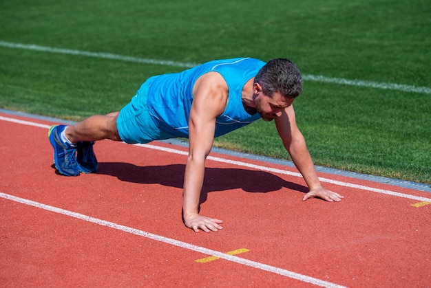 Muscoli forti. forza e potere maschile. sportivo in plancia. l'atleta fa flessioni. allenare i suoi muscoli centrali. uomo che fa esercizio di flessioni sullo stadio. palestra fitness all'aperto. allenamento muscolare atletico del ragazzo.