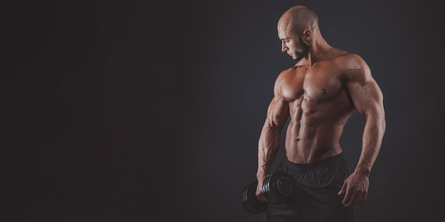 Muscoloso e in forma giovane bodybuilder fitness modello maschile in posa su sfondo nero copia spazio