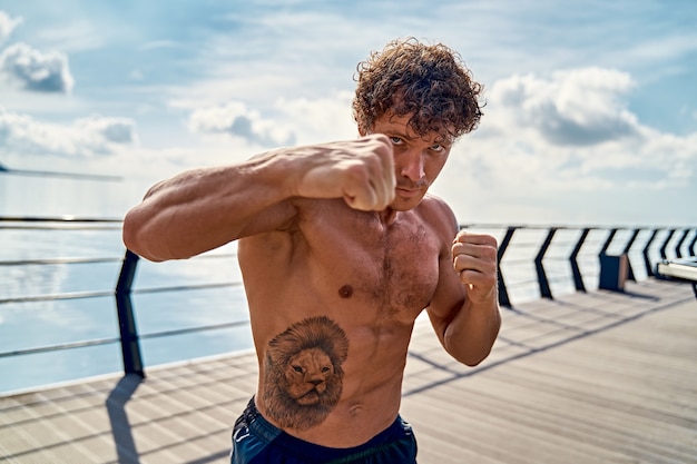 Muscoloso giovane atleta in piedi e praticando shadow boxing all'aperto la mattina presto sul molo