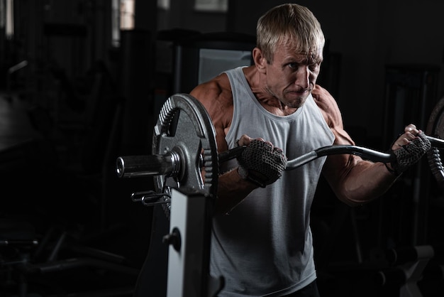 Muscoloso uomo brutale adulto con un barbell pompa le braccia in palestra Ritratto di autentico bodybuilder caucasico che fa esercizi di allenamento