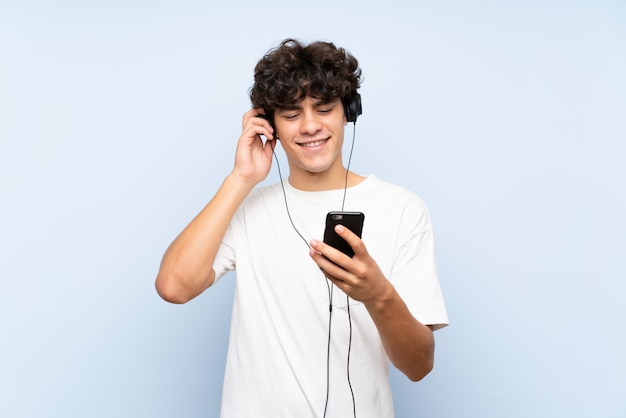 Musica d'ascolto del giovane con un cellulare sopra la parete blu isolata