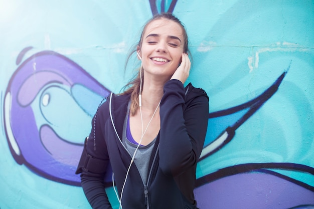 Musica d&#39;ascolto del pareggiatore femminile sul telefono cellulare davanti alla parete dei graffiti