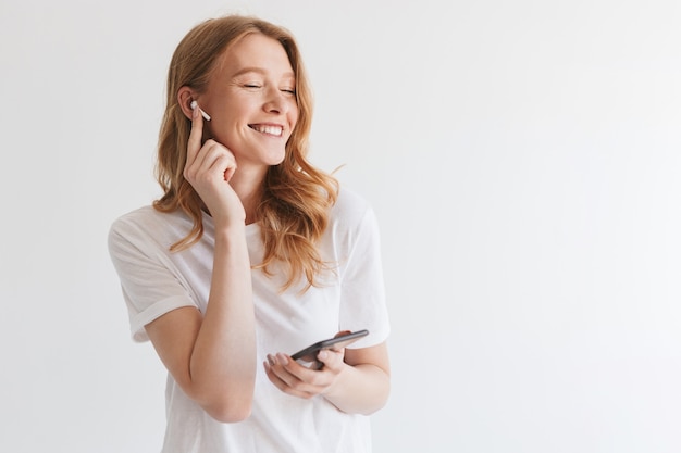 Musica d'ascolto della donna giovane rossa felice con gli auricolari dal telefono cellulare.