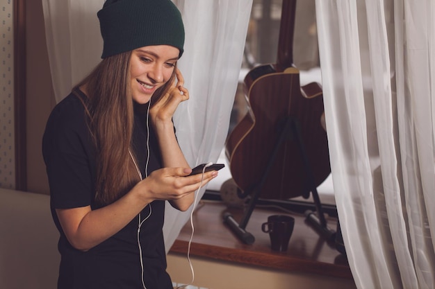 Musica d'ascolto della donna sveglia dei pantaloni a vita bassa vicino alla chitarra