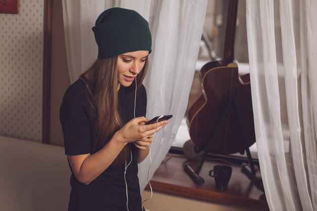 Musica d'ascolto della donna sveglia dei pantaloni a vita bassa vicino alla chitarra