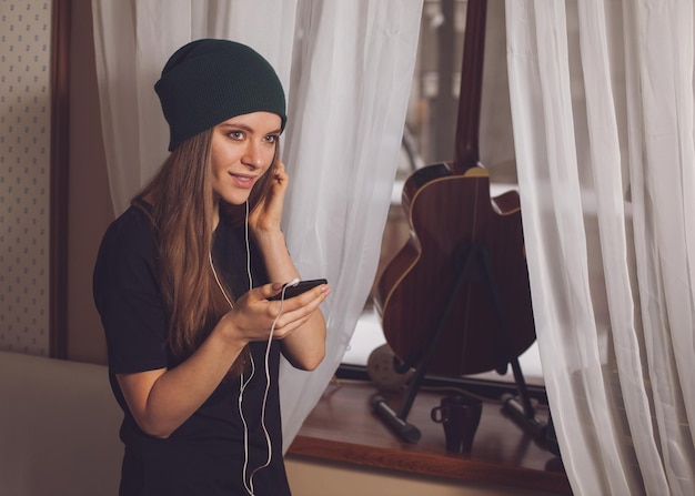 Musica d'ascolto della donna sveglia dei pantaloni a vita bassa vicino alla chitarra