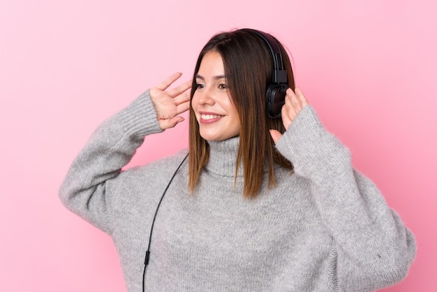 Musica d'ascolto della giovane donna con le cuffie sopra la parete rosa isolata