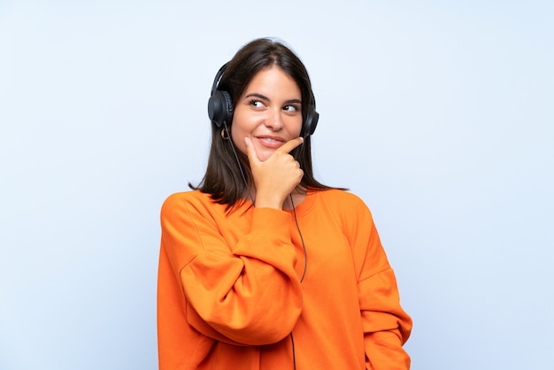 Musica d'ascolto della giovane donna con un cellulare sopra la parete blu isolata che pensa un'idea