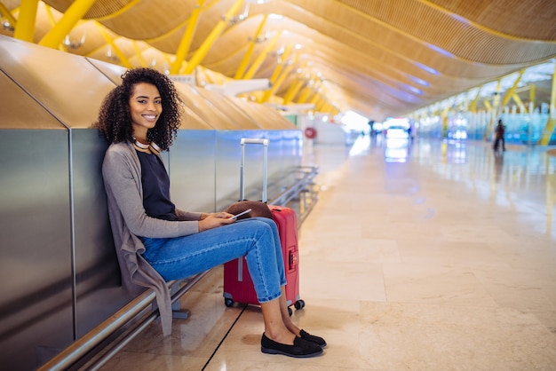 Musica d'ascolto della giovane donna di colore felice con le cuffie e il telefono cellulare all'aeroporto