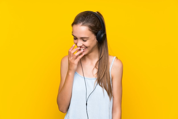 Musica d'ascolto della giovane donna sopra la parete gialla isolata che sorride molto