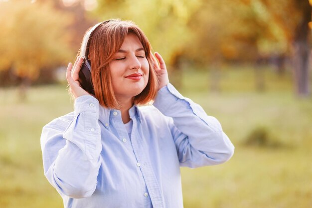 Musica d'ascolto della giovane donna sorridente con le cuffie alle cuffie nere senza fili della ragazza del tramonto