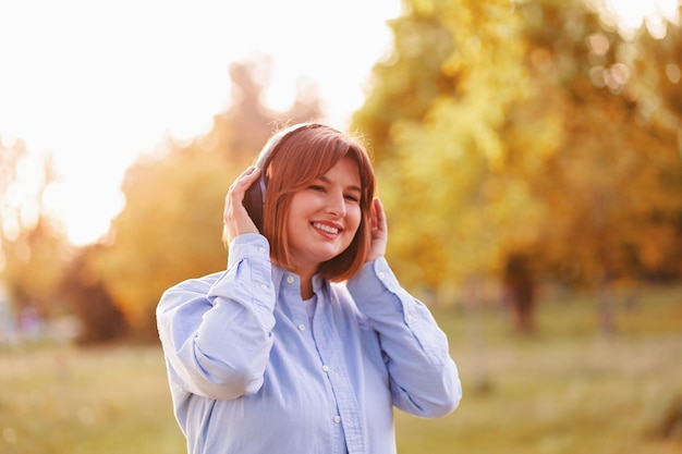 Musica d'ascolto della giovane donna sorridente con le cuffie alle cuffie nere senza fili della ragazza del tramonto