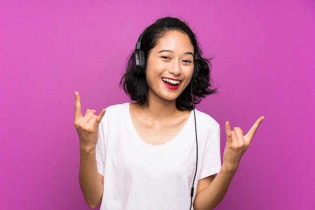 Musica d'ascolto della ragazza asiatica con un cellulare sopra la parete viola isolata