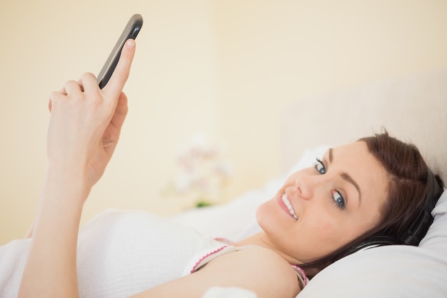 Musica d&#39;ascolto della ragazza felice sul suo smartphone che si trova sul letto