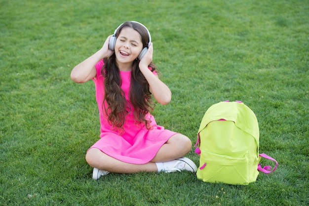 Musica d'ascolto delle cuffie della ragazza. Tempo piacevole. Le cuffie per bambini ascoltano musica. Tecnologia moderna. La scolaretta gode della melodia. Ascolta musica rilassante all'aperto. La ragazza del bambino gode del prato dell'erba verde della musica.