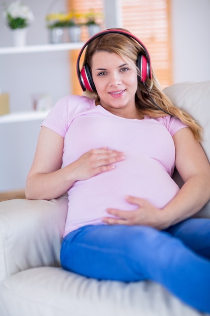 Musica d&#39;ascolto sorridente della donna incinta e toccante la sua pancia