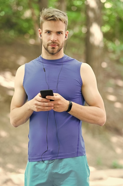 Musica migliore compagno per correre Atleta uomo sulla faccia occupata impostare la playlist sullo sfondo della natura Cuffie per allenamento sportivo ascoltare musica Una playlist corretta aiuta lo sportivo a correre o ad allenarsi meglio