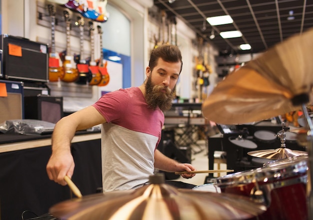 musica, vendita, persone, strumenti musicali e concetto di intrattenimento - musicista maschio che suona i piatti al negozio di musica