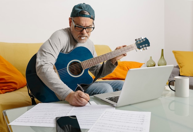 Musicista che suona la chitarra e compone musica in videoconferenza tramite il suo laptop