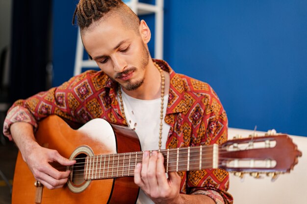 Musicista di giovane ragazzo elegante che suona la chitarra nel suo appartamento