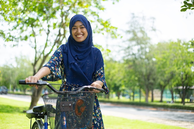 musulmano asiatico che tiene in bicicletta e sorride in giardino
