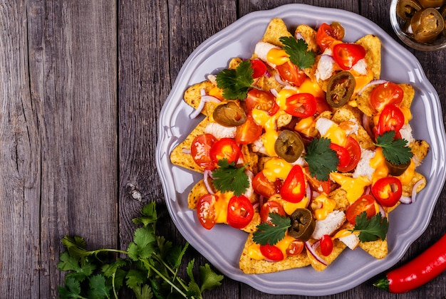 Nachos con salsa di formaggio fuso, jalapeno, pollo e verdure.