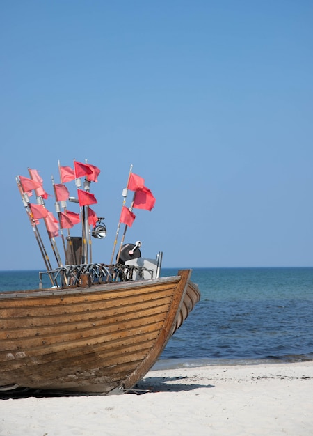 Naso della barca da pesca su una spiaggia sabbiosa con diverse piccole bandiere rosse su pennoni